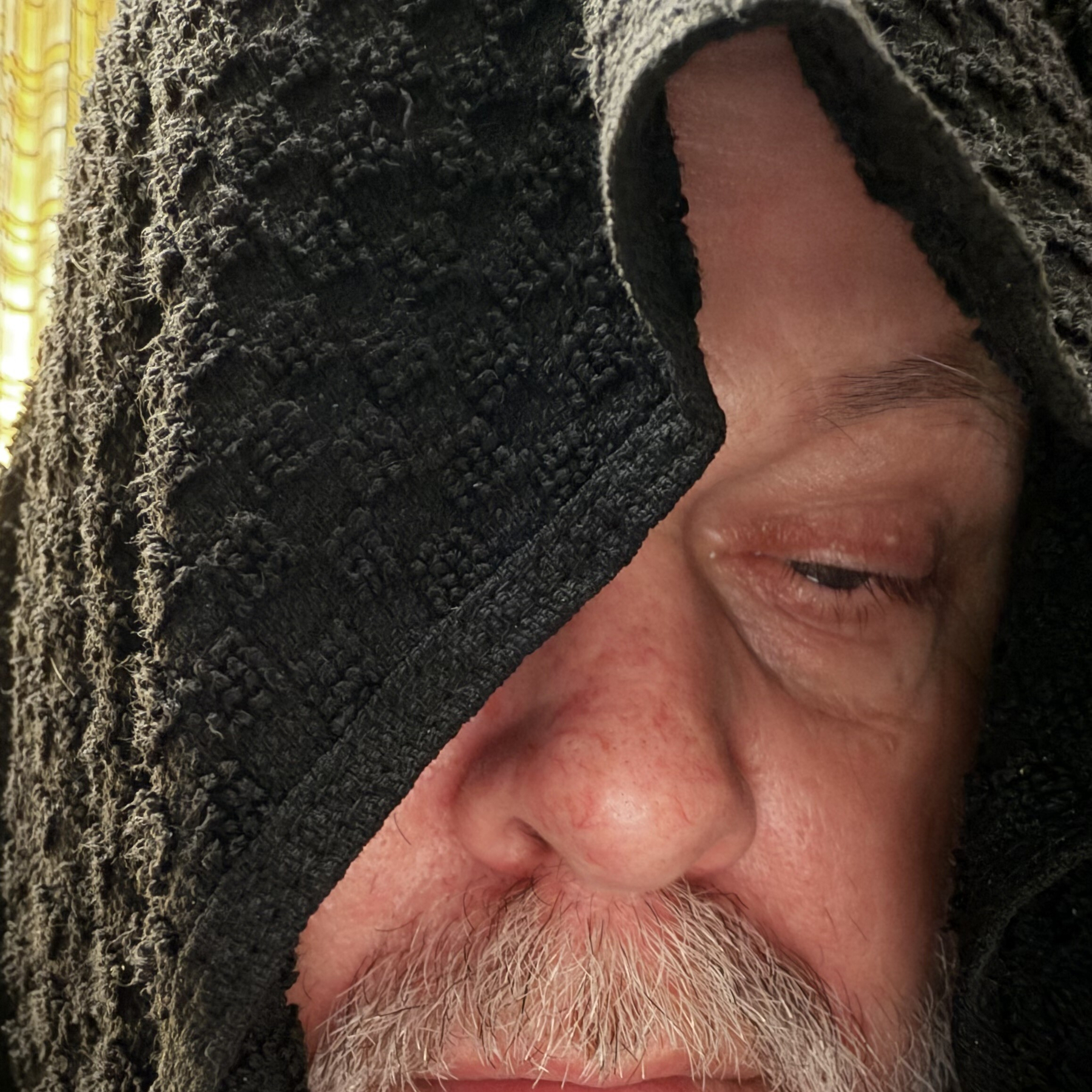 Auto-generated description: A close-up of a man's face partially covered by a textured dark towel with one eye closed.